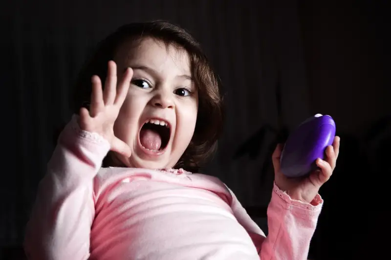 Niño asustado grita con la boca abierta, levantando una mano y sosteniendo un objeto morado.